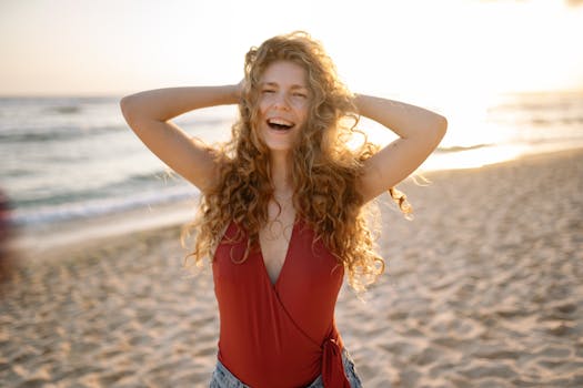 A happy woman with curly hair enjoys a sunny day on the beach, expressing freedom and joy.